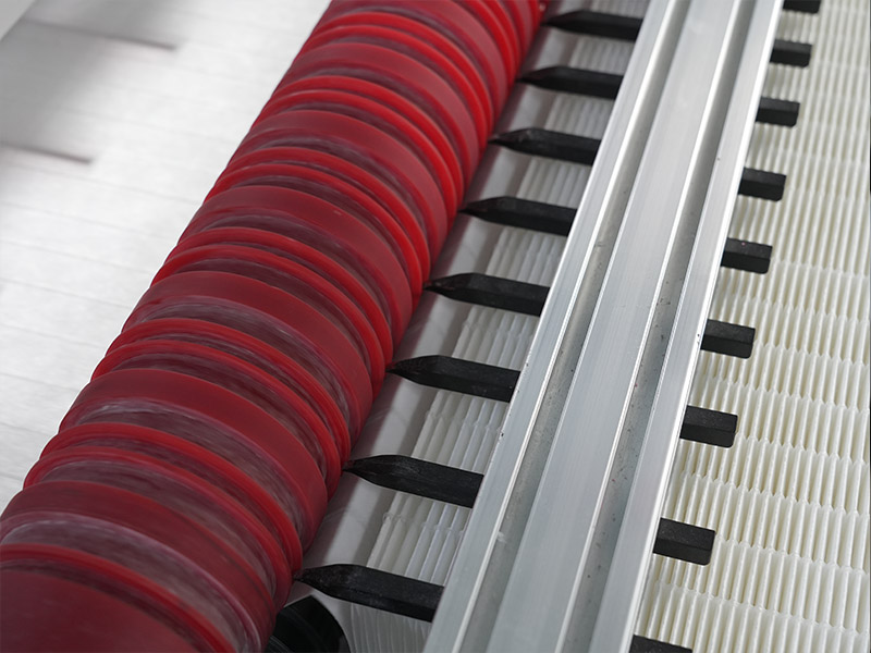 Close-up detail of automated pleating machine rollers guiding white air filter media for uniform spacing
