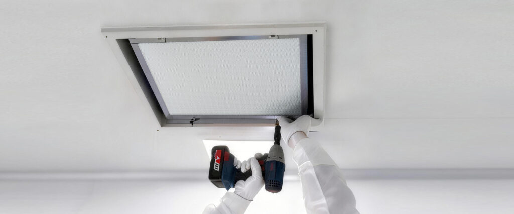 Technician installing a ceiling-mounted air filter panel using a cordless power drill